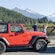 A convertible, 2 door utility vehicle parked near 2 people taking pictures of an Alaskan landscape